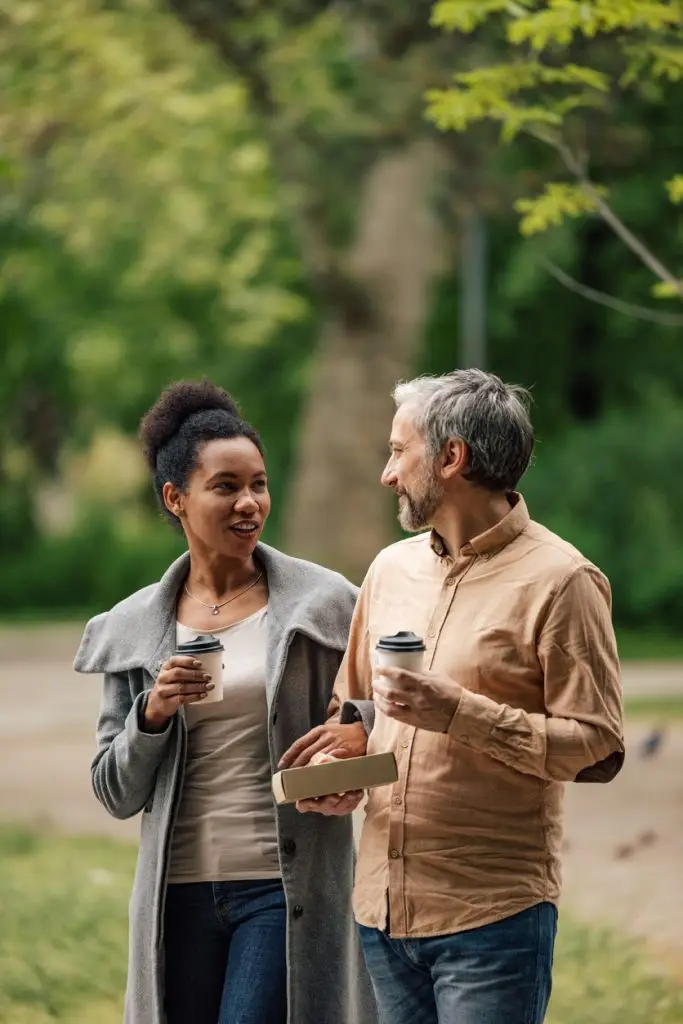 Adult couple, having a conversation, in a park, while drinking coffee.